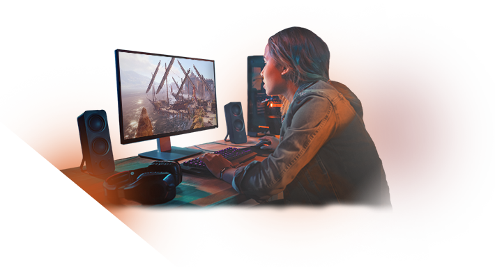 Persoon die druk bezig is met gamen, aan een bureau met een monitor waarop een game te zien is, luidsprekers aan weerszijden en zichtbare gaming-randapparatuur